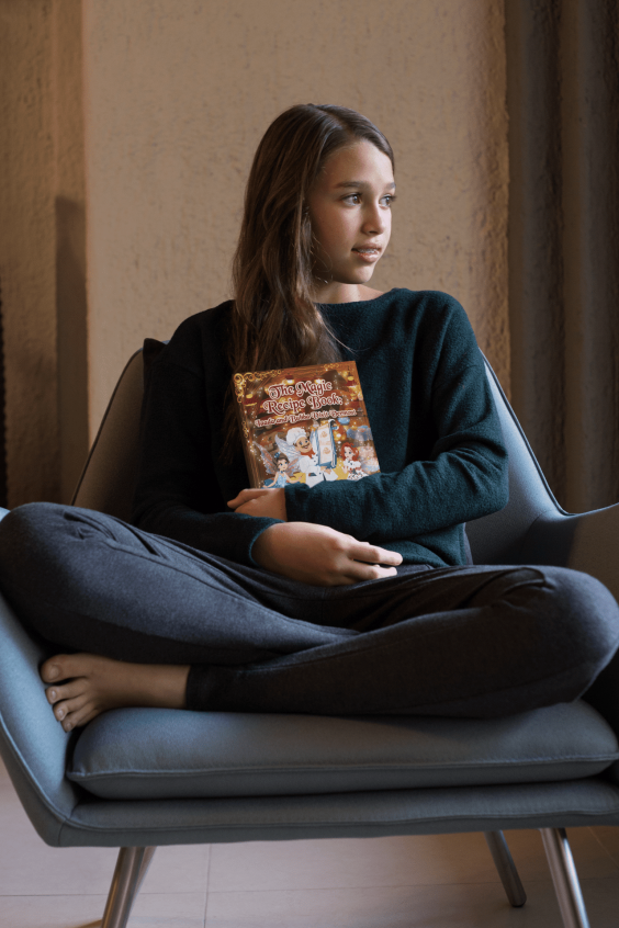 little-girl-holding-a-book-mockup-sitting-on-an-armchair-a19077-min